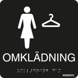 Svart taktil skylt med texten "OMKLÄDNING" med symbol och punktskrift – tillgänglig för synskadade.